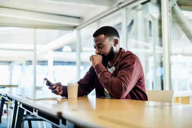 shot of a worried young businessman using a cellphone in a modern office - waiting telephone on the phone anxiety imagens e fotografias de stock