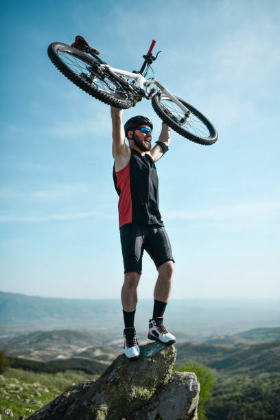 istock Smiling Male Cyclist Lifting Bicycle In Air On Highest Mountain Point 1335901385