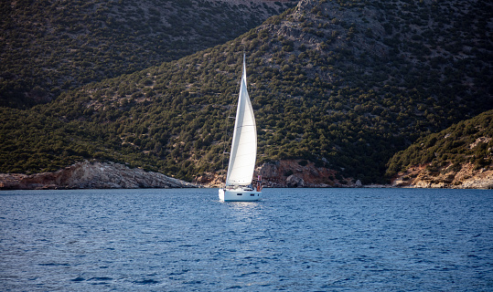 Sailboat with open white sails cruising in transparent ripple Aegean sea landscape background, summer sunny day. Destination for vacation swim sunbathe relaxation Kimolos island, Cyclades Greece.