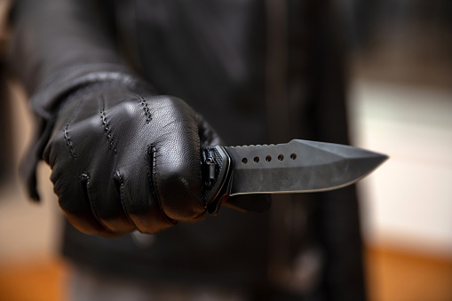 Robber threaten with a dagger, blur background, closeup view. Burglar  holding a knife in gloved hand, armed robbery concept.