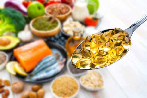 Omega-3 capsules and healthy food Close up view of a metal spoon filled with Omega-3 capsules shot against defocused food rich in Omega-3 acid like salmon, sardines, avocado, and nuts. omega 3 stock pictures, royalty-free photos & images