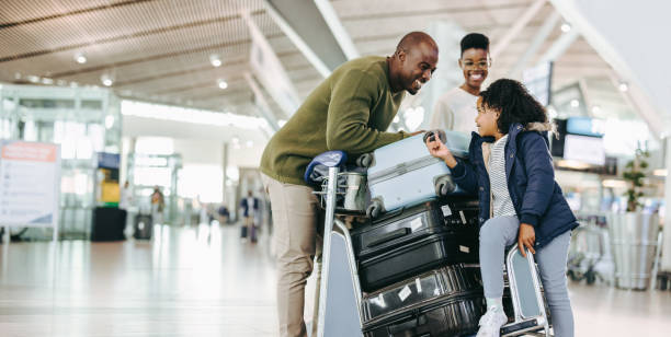 tourist family with luggage trolley at airport - reizen stockfoto's en -beelden
