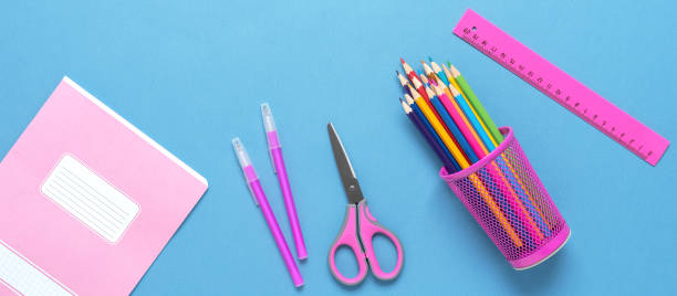 istock Stationery on a blue paper background, wide composition. Colored pencils, pens, ruler, scissors and a notebook. Top view, flat lay. Banner. Back to school. 1335921537