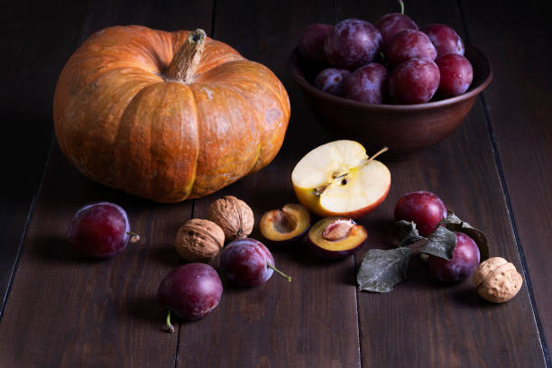 Still life with autumn fruits. Fresh ripe plums, pumpkin, apple and walnuts on a dark wooden surface. Rustic style. Harvest, autumn, healthy and vegetarian food concept. Selective focus.