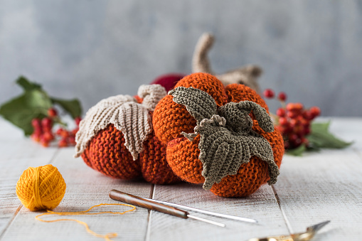 Cute soft colorful knitted pumpkins with leaves crochets scissors and yellow threads ball on white wooden table close view