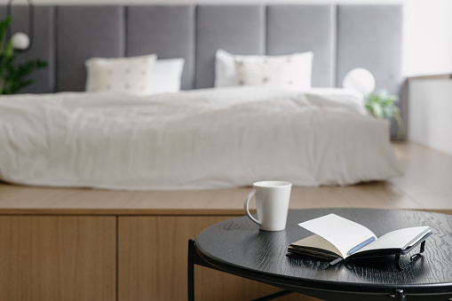 Home bedroom interior, white bed decor. Cozy room with scandinavian design, closeup at coffee table near white bed. Furniture for comfortable relaxation, apartment with wooden object.