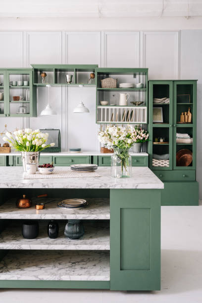New modern kitchen with green vintage furniture Kitchen with green vintage furniture, marble countertop with flowers and bowl of cherries, bucket with tulips, cupboard with various mugs, crockery and devices. Vertical shot hygge photos stock pictures, royalty-free photos & images