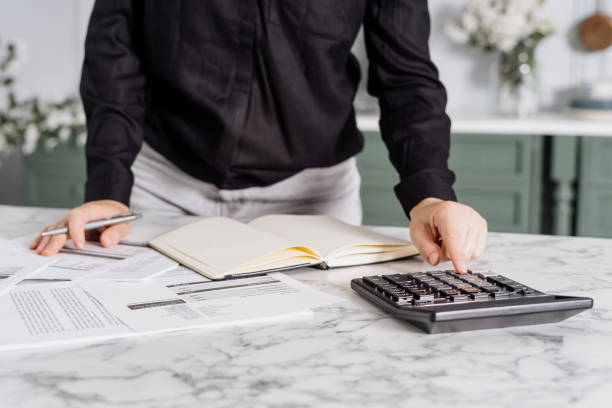 istock Person typing costs in calculator in kitchen 1335927440