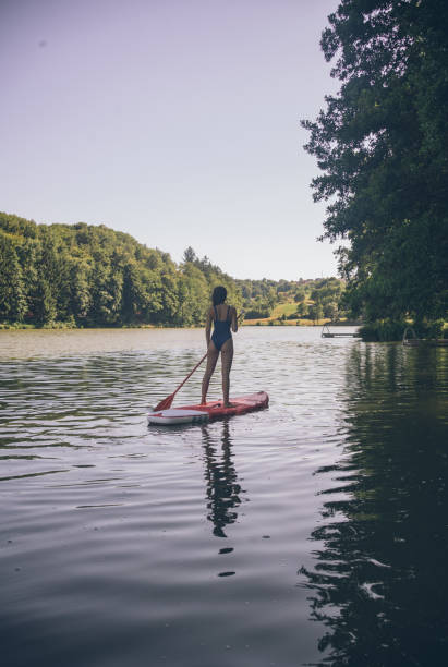 istock View of young woman paddle boarding down lake 1335928450