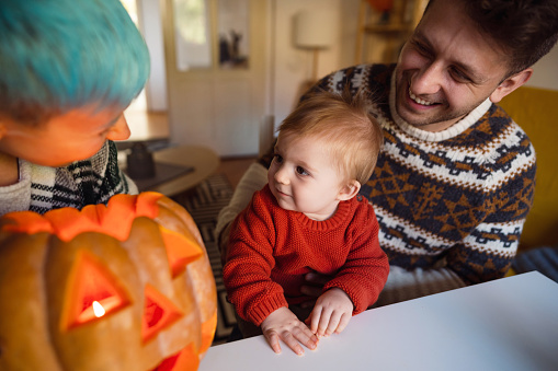 Happy young Caucasian family of three having fun while decorating a pumpkin for the Halloween holiday.