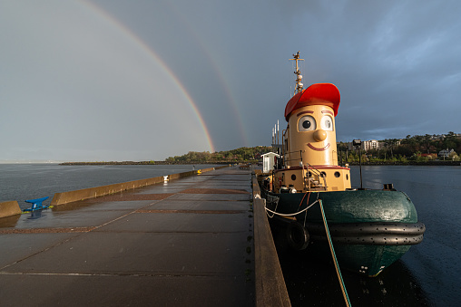 May 18, 2021 - Theodore Tugboat, a children's television show character produced by CBC, docked on the Bedford Basin beneath a bright rainbow following a heavy thunderstorm.