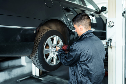 Replacing summer tires for winter using pneumatic wrench tool by mechanic worker after balancing wheels in car service garage shop. Car service, repair and maintenance concept - auto mechanic man with electric screwdriver changing tire in auto repair shop.