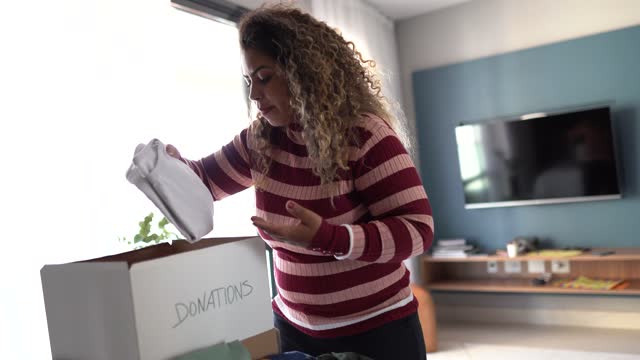 Woman putting clothes for donation in a box at home