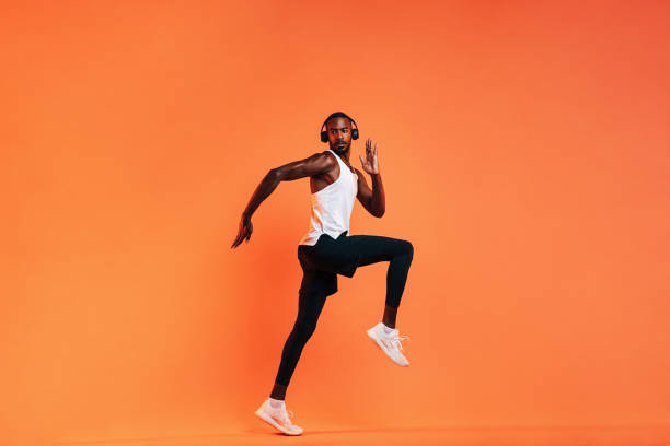 istock Young athlete in wireless headphones doing intense workout in studio over orange background 1335957275