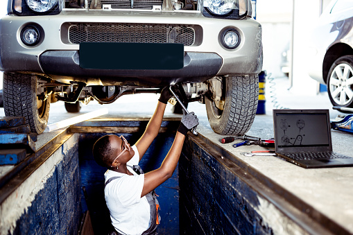 Female Black Mechanic examining under the car at the repair garage
