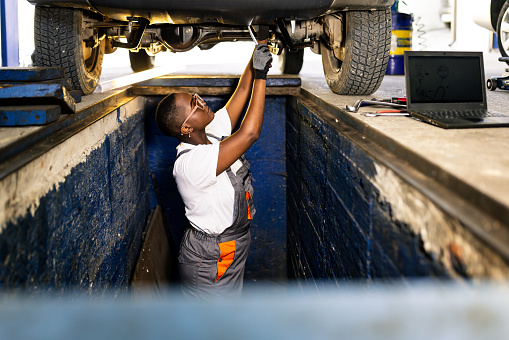 Female Black Mechanic examining under the car at the repair garage