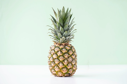 Single pineapple on a white table in front of a green  wall.