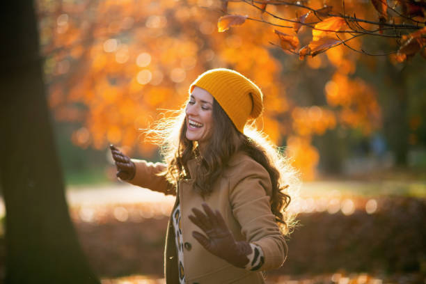 smiling stylish woman in brown coat and yellow hat dancing stock photo