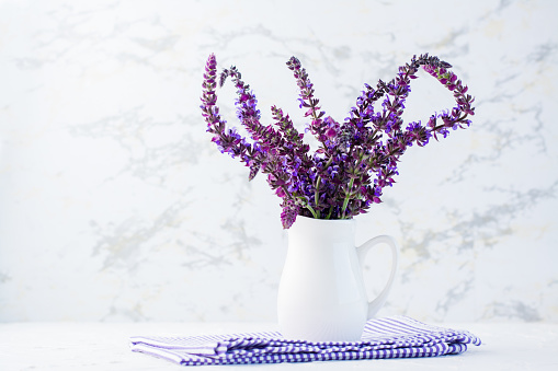 A bouquet of fresh fragrant lavender in a white jug on the table. White and purple colors. Home decoration. Copy space