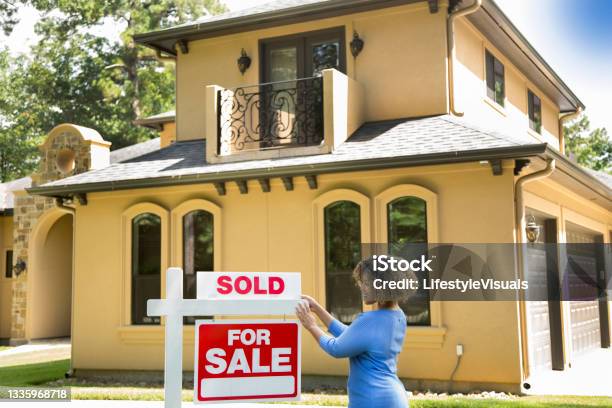 Lovely Young Adult Real Estate Agent Standing Beside Her For Sale Sign In Front Yard Of Home She Adds The Sold Sign And Wears A Blue Top And Jeans Stock Photo - Download Image Now