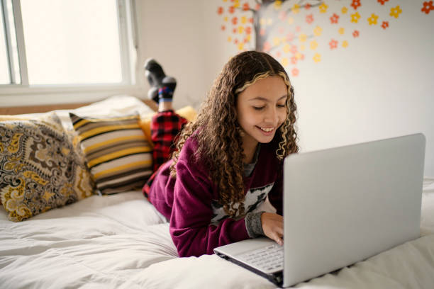 Teen girl using laptop in bed. Using social media or studying. stock photo