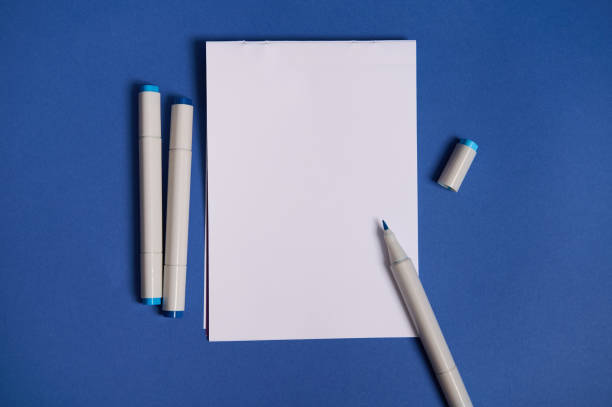 istock Dichromatic flat lay composition with watercolor markers or felt-tip pens with a white blank empty paper sheet with copy space, isolated on blue background. 1335969993