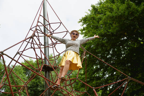 Senior woman, 67 years old, with dyed pink hair hair is standing on climbing frame of a playground, she is , wearing a golden skirt and a shirt with  leopard  print pattern, one arm is raised