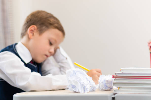 istock A cute boy first grader in a school uniform does homework while sitting at a desk with a pencil in his hands at home. Remote education. Selective focus. Close-up 1335973714