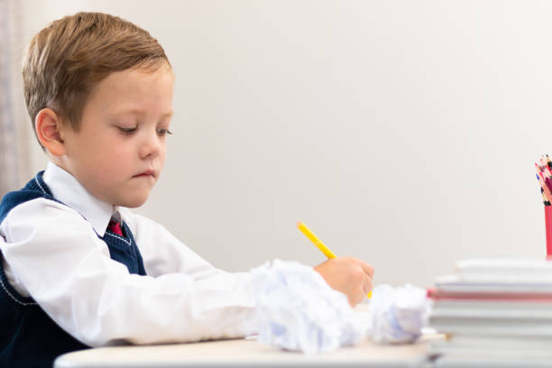 istock A cute boy first grader in a school uniform does homework while sitting at a desk with a pencil in his hands at home. Remote education. Selective focus. Close-up 1335973715
