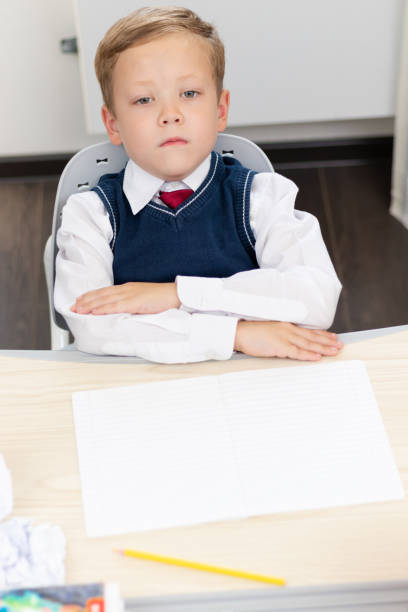 istock A cute boy first grader in a school uniform and a tie at home during a pandemic does homework while sitting at his desk. Selective focus. Close-up 1335973721