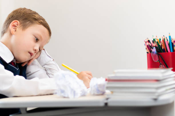 istock A cute boy first grader in a school uniform does homework while sitting at a desk with a pencil in his hands at home. Remote education. Selective focus. Close-up 1335973726