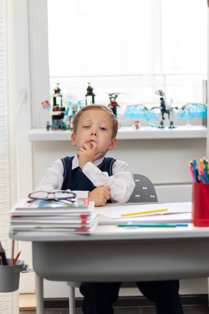 istock Cute boy first grader in school uniform at home during a break fooling around while sitting at his desk. Selective focus. Close-up 1335973735