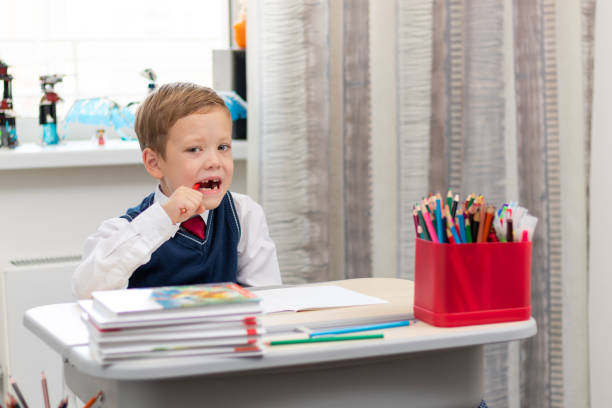 istock A cute boy first grader in a school uniform does homework while sitting at a desk with a pencil in his hands at home. Remote education. Selective focus. Close-up 1335973754