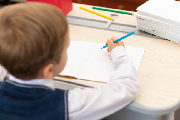 istock A cute boy first grader in a school uniform does homework while sitting at a desk with a pencil in his hands at home. Remote education. Selective focus. Close-up 1335973762