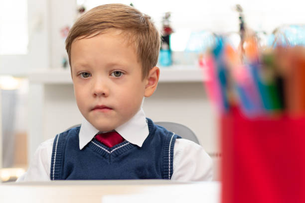 istock A cute boy first grader in a school uniform and a tie at home during a pandemic does homework while sitting at his desk. Selective focus. Close-up 1335973765