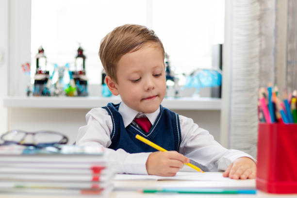istock A cute boy first grader in a school uniform does homework while sitting at a desk with a pencil in his hands at home. Remote education. Selective focus. Close-up 1335973777