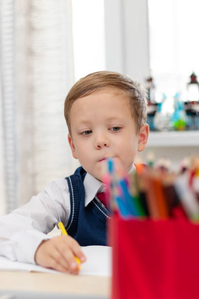 istock A cute boy first grader in a school uniform does homework while sitting at a desk with a pencil in his hands at home. Remote education. Selective focus. Close-up 1335973781