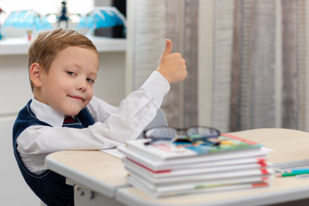 istock Cute boy first grader in school uniform at home during a break fooling around while sitting at his desk. Selective focus. Close-up 1335973799