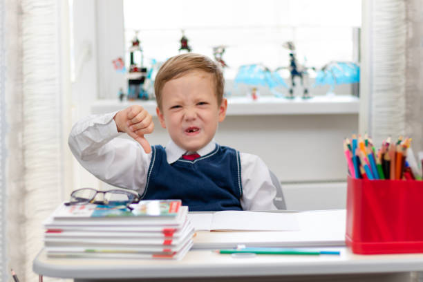 istock Cute boy first grader in school uniform at home during a break fooling around while sitting at his desk. Selective focus. Close-up 1335973800