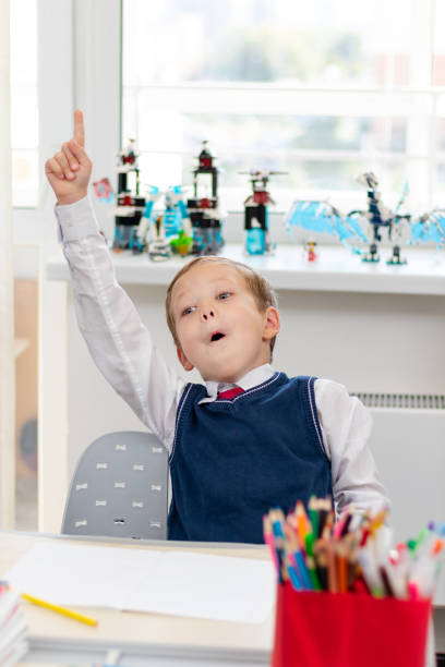 Cute boy first grader in school uniform at home during a break fooling around while sitting at his desk. Selective focus. Close-up