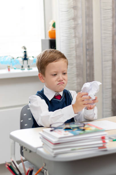 istock Cute boy first grader in school uniform at home during a break fooling around while sitting at his desk. Selective focus. Close-up 1335973814