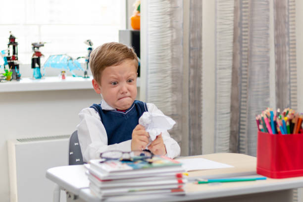 istock Cute boy first grader in school uniform at home during a break fooling around while sitting at his desk. Selective focus. Close-up 1335973818