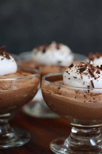 istock Image of three glasses containing home-made chocolate mousse dessert topped with piped whipped cream and grated chocolate, wood grain surface, black background, focus on foreground 1335975013
