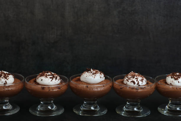 istock Image of glasses in a row containing home-made chocolate mousse dessert topped with piped whipped cream and grated chocolate, black background, focus on foreground, copy space 1335975079