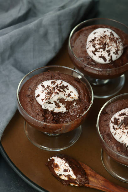 istock Image of three glasses containing home-made chocolate mousse dessert topped with piped whipped cream and grated chocolate on tray, grey muslin, black background, elevated view 1335975113