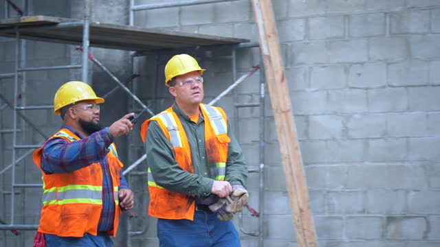Two construction workers at job site walking, talking