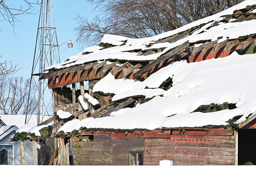 Roof of old barn crumbling while covered with snow.