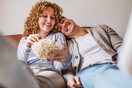 Young couple relaxing at home while watching a movie and eating popcorn