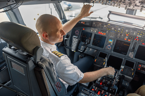 High angle view of professional pilot sitting in an airplane cabin, ready for takeoff. Aircraft, aircrew, occupation concept