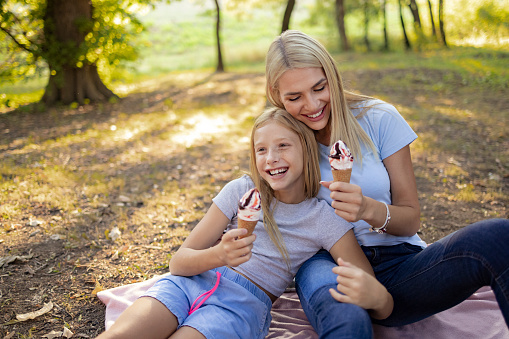Caucasian family having fun together in nature, a mother with her young daughter, having an ice cream together and smiling